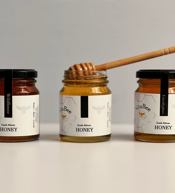 Three VitaBee honey jars: Wildflower, Citrus and Eucalyptus, with a wooden honey dipper