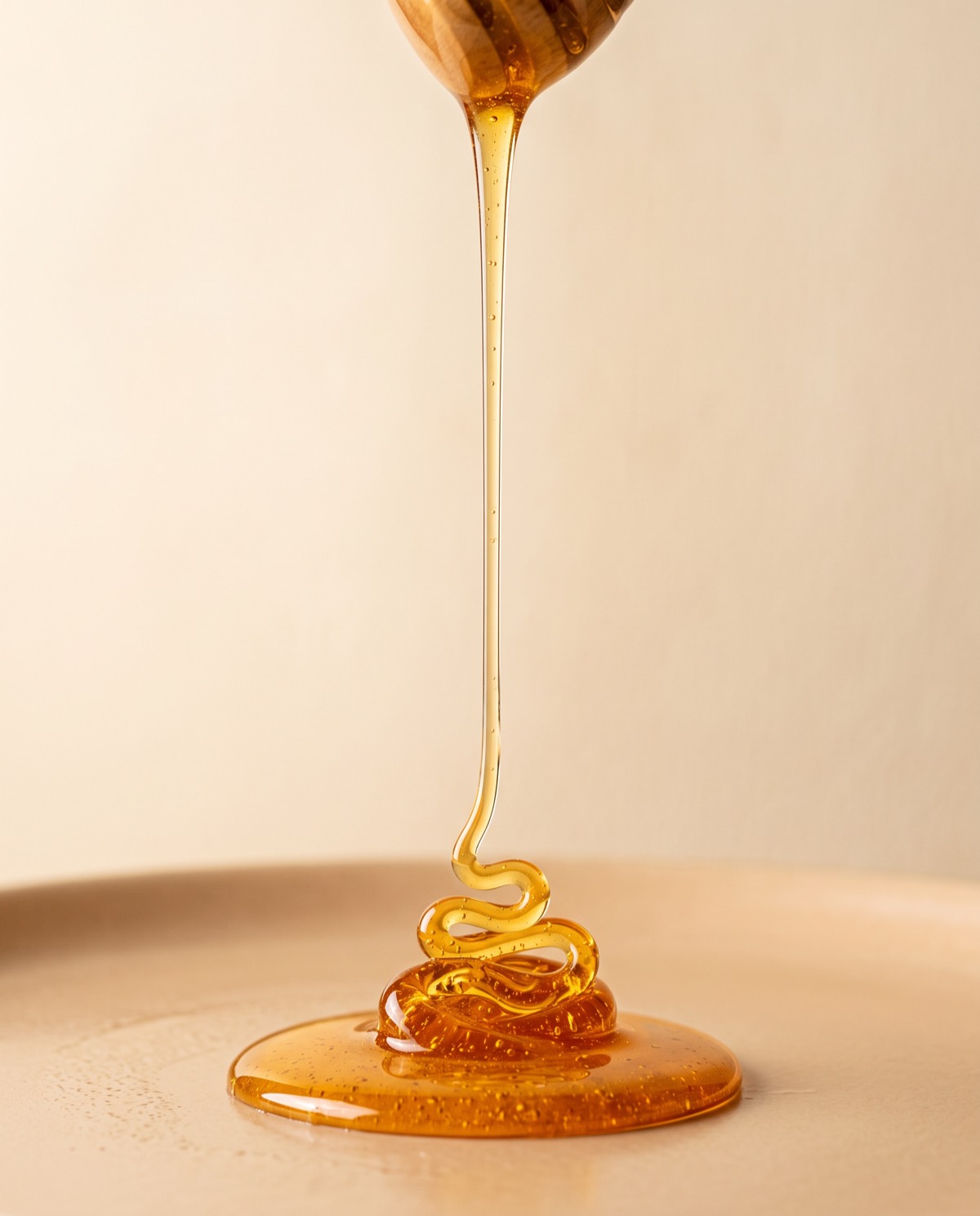 A thread of raw golden honey falling from a wooden honey dipper